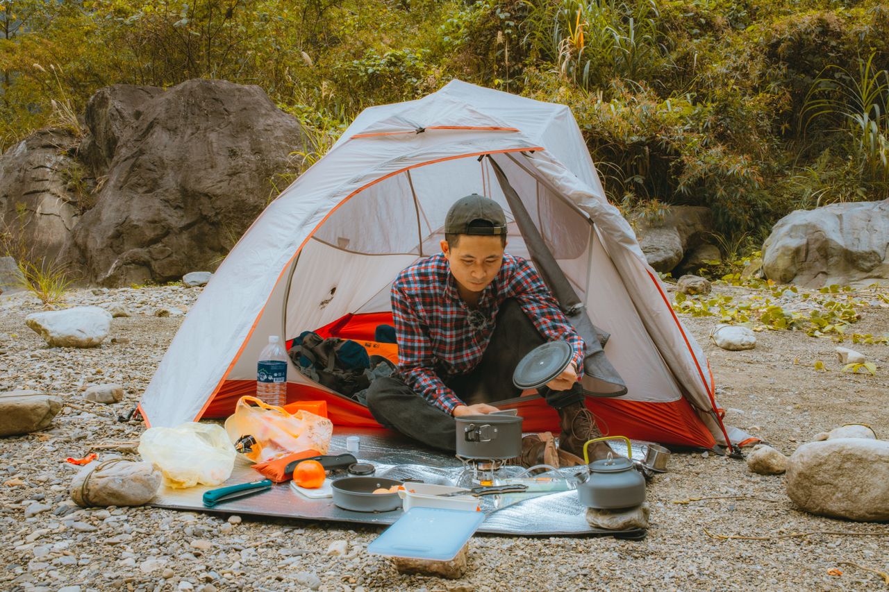 A young man enjoys a camping experience with a tent and cooking gear in a scenic outdoor area.